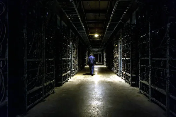 A technician walking away down the single lit aisle of a powered-down cryptocurrency mining hall.