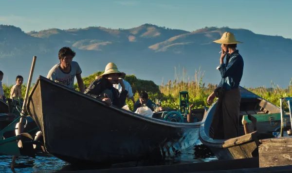 Women in conical hats crossing Inle Lake by wooden boat, mountains behind.
