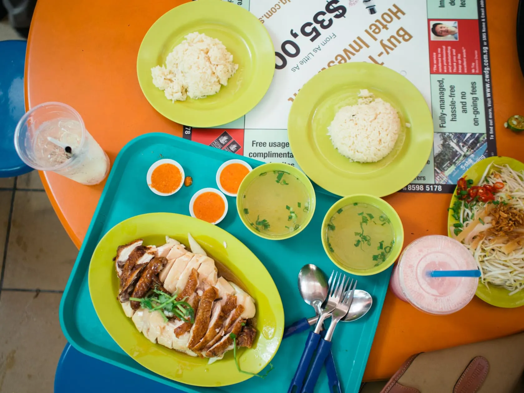half Top-down spread of Hainanese chicken rice, chilli sauces, soup and bean sprouts on hawker trays at Maxwell Food Centre