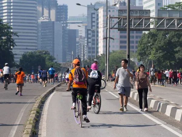 Crowds on Sudirman boulevard during Jakarta car-free day, city towers behind.